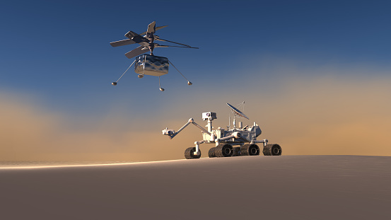 Technological teamwork on Mars. Perseverance Rover and Ingenuity Mars Helicopter working together for new researches and discoveries. New Mars explorer drone helicopter Ingenuity flying on Mars ground for new discoveries. The Mars Helicopter, Ingenuity, is a technology demonstration to test powered, controlled flight on another world for the first time. It hitched a ride to Mars on the Perseverance rover. Ingenuity is new space drone. The vehicle, caught in a sandstorm during the flight, lands on the ground.