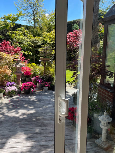 istock Image of sliding patio doors opening onto whitewashed, grooved timber decking, view  of potted flowering plants, green mown lawn, Japanese maples, stone lanterns and garden statue ornaments, clear blue, sunny sky 1321882652