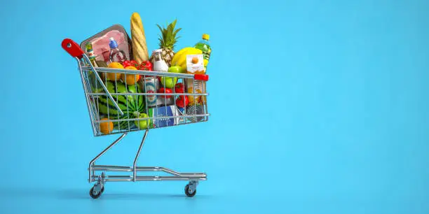 Photo of Shopping cart full of food on blue background. Grocery and food store concept.