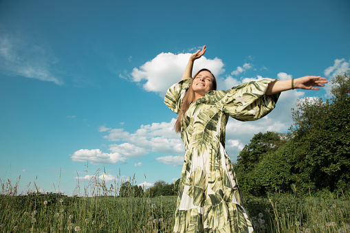 young woman in green field with hands outstretched towards blue sky, happiness