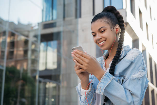 istock African American woman using mobile phone, communication, looking at digital screen, walking on the street. Stylish hipster girl holding smartphone, listening to music 1321890739