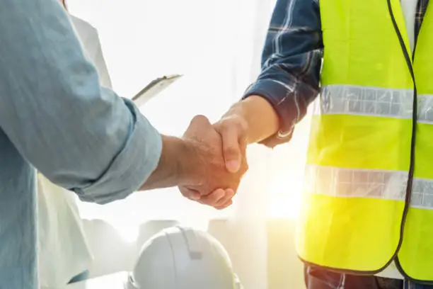 Photo of Contractor. construction worker team hands shaking after plan project contract on workplace desk in meeting room office at construction site, contractor, engineering, partnership, construction concept