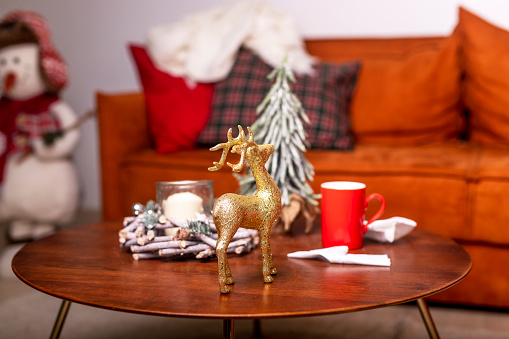 Golden reindeer, red mug on coffee table in living room interior with christmas decoration and toys.