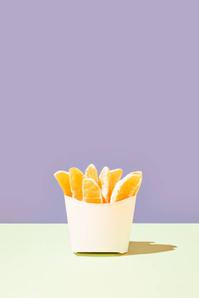 Creative diet idea, fresh organic orange slices in fast food french fries bag on bright pastel background. Modern minimalistic summer concept. Healthy eating composition, vertical copy space arrangement. idea creativa de la dieta, rodajas de naranja orgánica frescas en la bolsa de patatas fritas de comida rápida sobre fondo pastel brillante. concepto de verano minimalista moderno. composición de alimentación saludable, disposición vertical del espacio