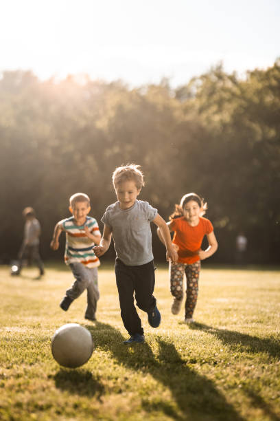 children playing soccer outdoors - elementary age child group of people togetherness imagens e fotografias de stock