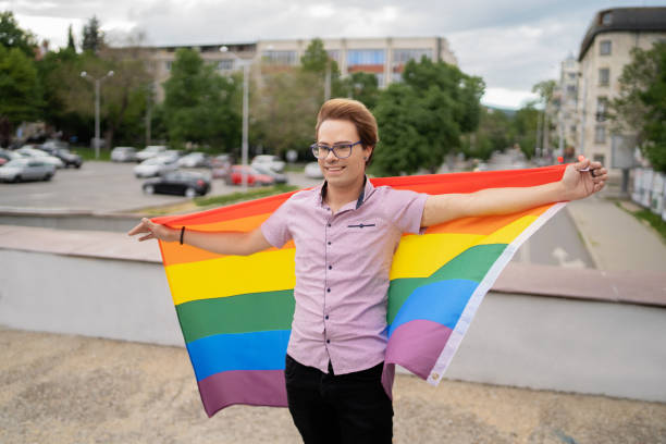 istock A gay man holding the rainbow flag bihind his back and looking forward 1321907328