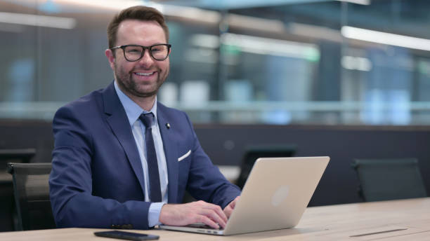 istock Middle Aged Businessman with Laptop Smiling at Camera 1321907729