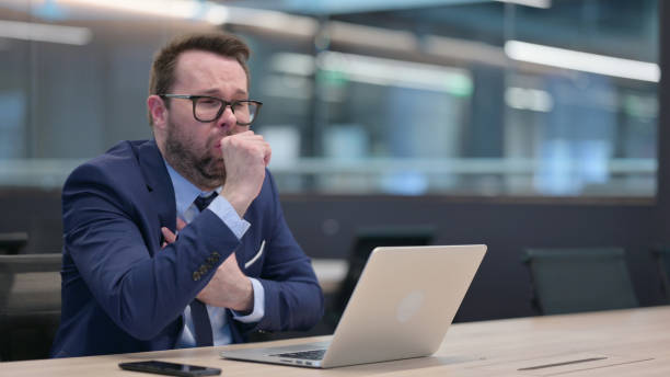 istock Middle Aged Businessman with Laptop Coughing 1321908274