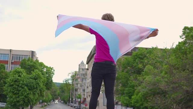 A transgender man holding the transgender flag  with the back to the camera