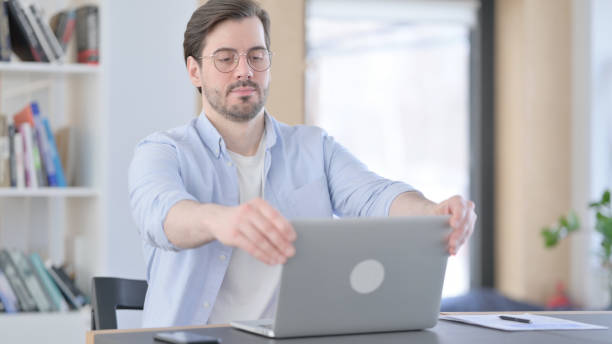 istock Man in Glasses Closing Laptop Going Away from Office 1321917590