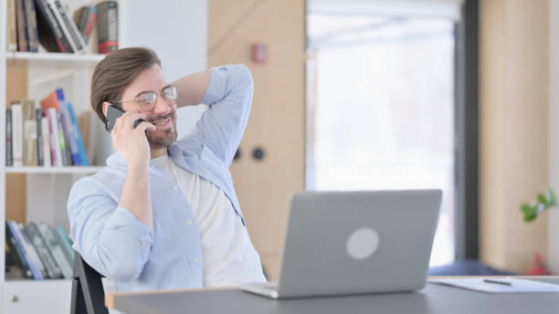 istock Man in Glasses with Laptop using Smartphone in Office 1321917668