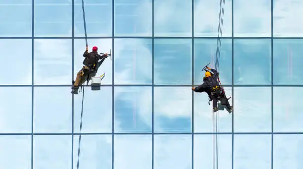 Photo of Group of workers cleaning windows service on high rise building. Workers cleaning glass curtain wall. Special job concept, panoramic view