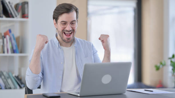 istock Successful Man in Glasses Celebrating on Laptop in Office 1321921652
