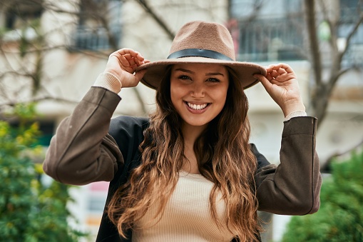 Young hispanic tourist woman smiling happy holding hat at the city.
