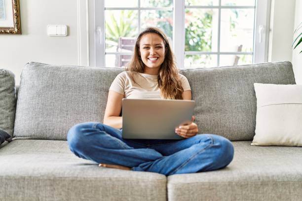istock Beautiful young brunette woman sitting on the sofa using computer laptop at home with a happy and cool smile on face. lucky person. 1321930368