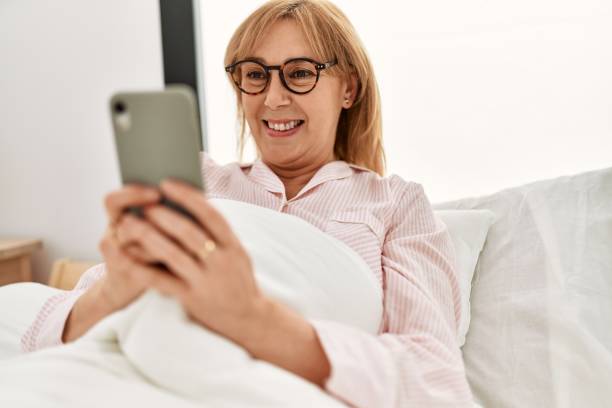 istock Middle age blonde woman using smartphone lying on the bed at home. 1321931051