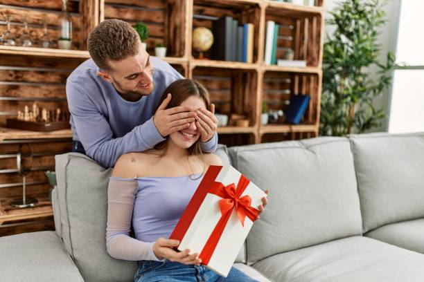 istock Young man surprising his girlfriend with birthday gift at home. 1321931303