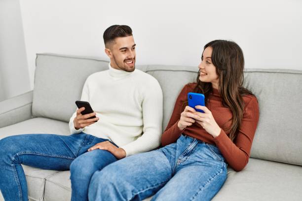 istock Young hispanic couple using smartphone sitting on the sofa at home. 1321931555