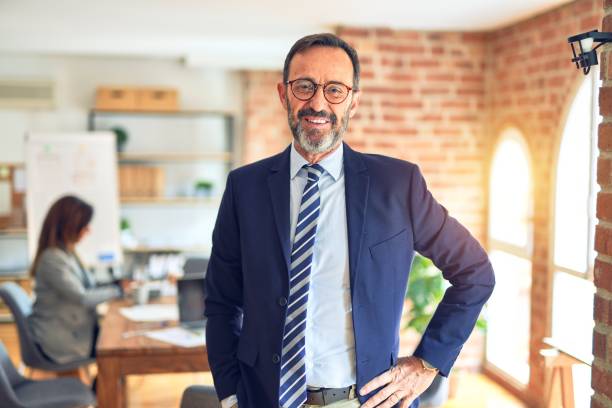 empresario de mediana edad sonriendo feliz y confiado. de pie con sonrisa en la cara trabajando con socia empresaria en la oficina - 50 59 años fotografías e imágenes de stock