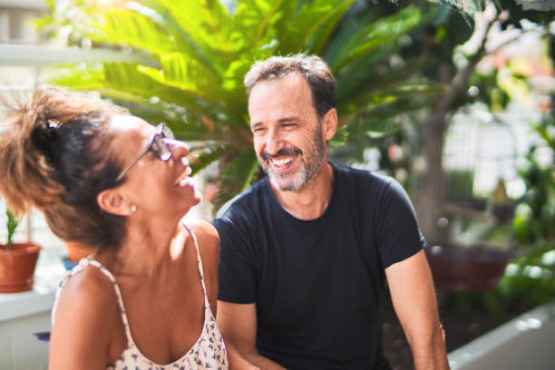 mediana edad hermosa pareja sentada en la terraza hablando y sonriendo - mature adult couple caucasian outdoors fotografías e imágenes de stock