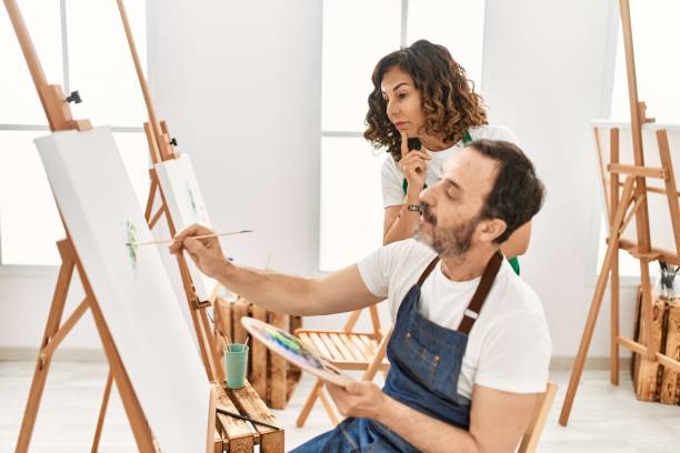 istock Middle age student and teacher with serious expression painting at art school. 1321935054