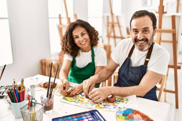 Two middle age students smiling happy modeling clay sitting on the table at art school.