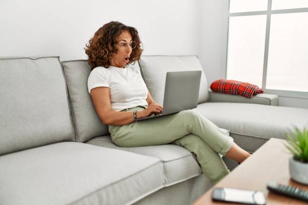 istock Middle age hispanic woman working using computer laptop at home scared and amazed with open mouth for surprise, disbelief face 1321935778