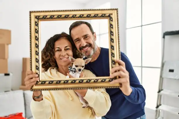 Middle age hispanic family smiling happy holding empty frame at new home.