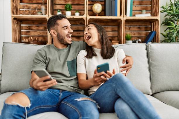 istock Young latin couple using smartphone sitting on the sofa at home. 1321937224