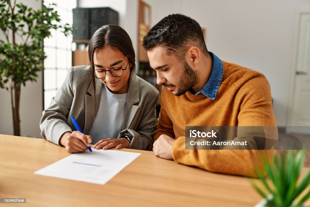 Couple smiling happy signing contract at the office. Couple smiling happy reading document at the office. Signing Stock Photo