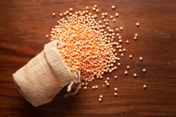 close-up of organic masoor dal (lens culinaris) or whole pink dal spilled out from a laying jute bag over wooden brown background. - lentil full frame macro close up imagens e fotografias de stock