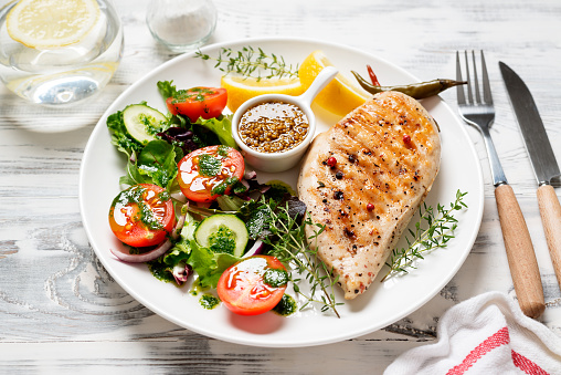 Grilled chicken breast with fresh vegetable salad. Healthy food, keto diet, diet lunch concept.  White wooden background.