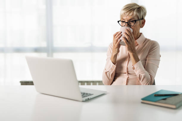 istock Smiling businesswoman drinking coffee while working on laptop in the office 1321968285