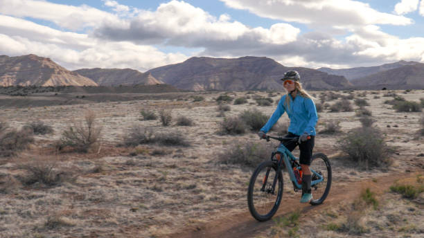 istock Young woman mountain bikes along trail through desert 1321982968