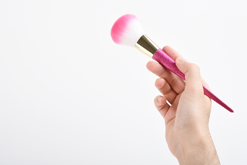 Man hand holding a glitter pink color make-up brush on the white background with copy space