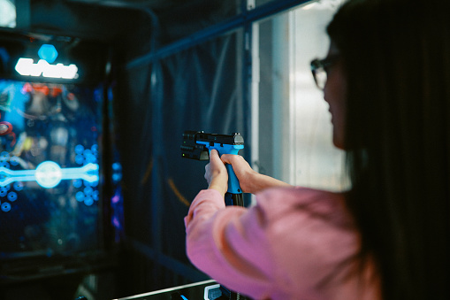 Woman in the video games arcade, playing a shooter game simulation.