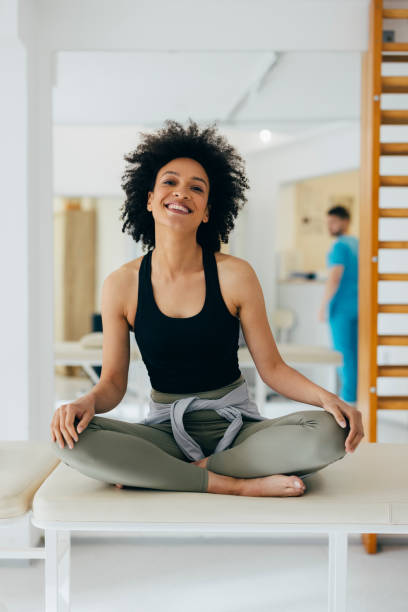 병원 침대에서 앉아 카메라를 보고 웃고 있는 아프리카계 미국인 여성의 초상화 - torso physical therapy patient relaxation exercise 뉴스 사진 이미지