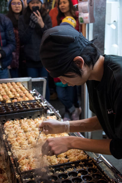 Vendor making takoyaki on a takoyaki pan in Osaka, Japan Osaka, Japan- 27 Nov, 2019: Vendor making takoyaki on a takoyaki pan in Osaka, Japan. Takoyaki is famous street food in Osaka. cooking takoyaki is a ball shaped japanese snack stock pictures, royalty-free photos & images