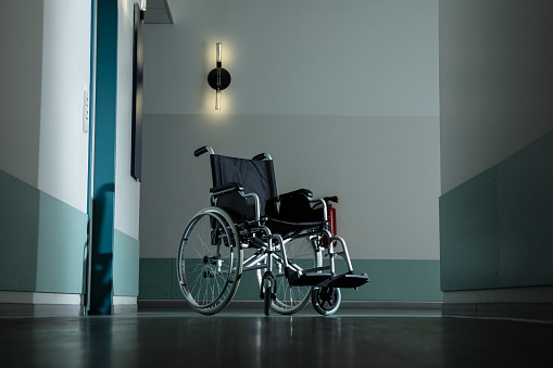 Silhouette Of Empty Wheelchair Parked In Hospital Corridor