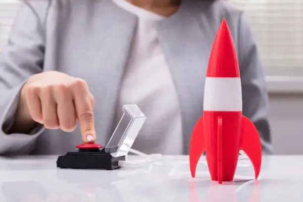 Businesswoman's Hand Launching Rocket By Pressing Red Button