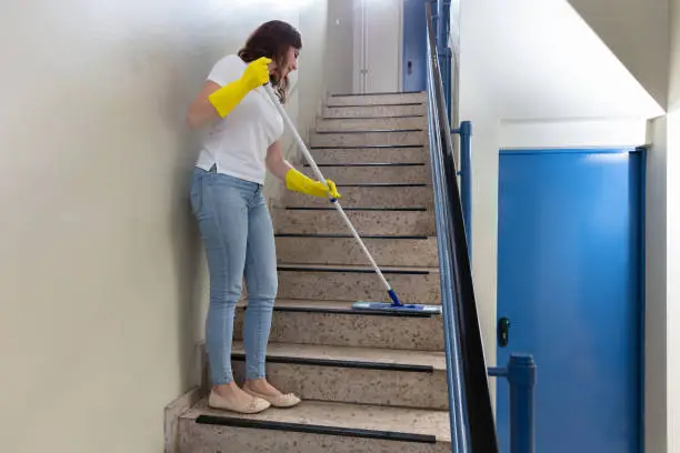Young Female Janitor Cleaning Staircase With Mop