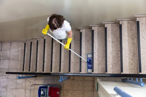 Young Female Janitor Cleaning Staircase With Mop