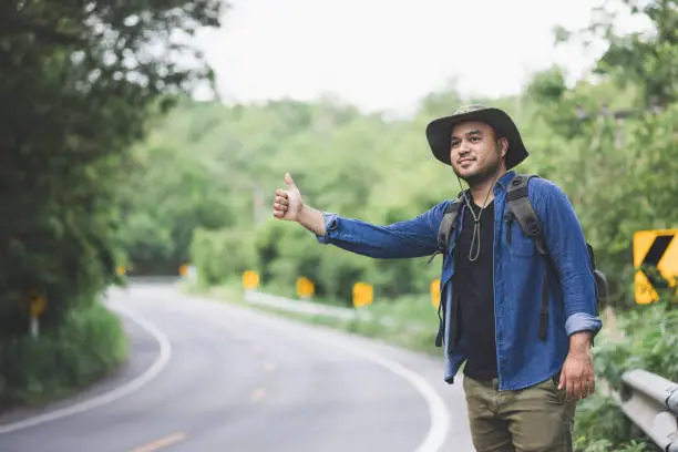 Photo of Pick me up. Man hitchhiking on the side of the road. Man try stop car thumb up. Hitchhiking one of cheapest ways traveling.