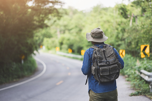Young handsome man with a backpack is walking alone the road. Man is looking forward to an interesting travelling.