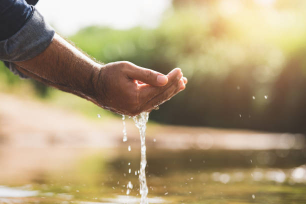 istock Closeup water drops falling down from man hand at river in mountains.Hand touching fresh water. 1322066982