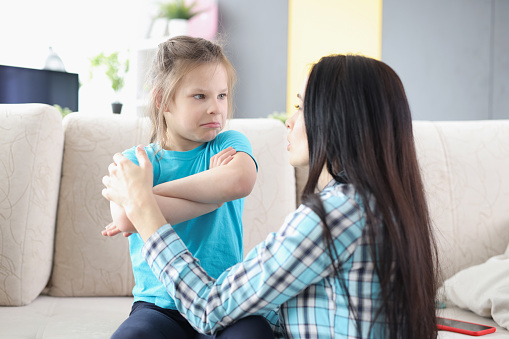 Sad offended daughter sitting on couch, turning back to mother after quarrel at home. Family misunderstanding and childhood problems.