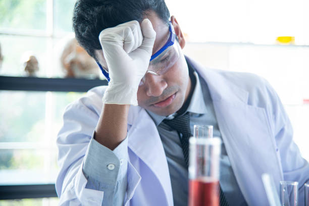 Los jóvenes científicos o investigadores usan anteojos haciendo investigación química en laboratorio. Científico cansado y estresado trabajando en equipos de laboratorio. - foto de stock