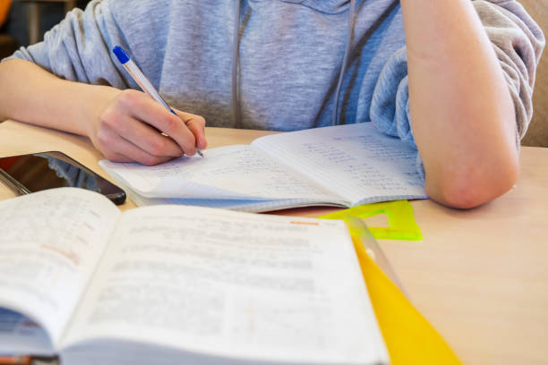 istock Teenage boy writes with a pen in a notebook while sitting at the table, concentrating on his homework before exams. 1322077892