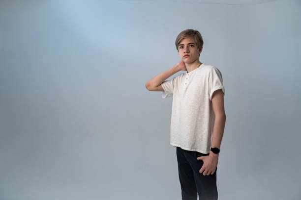 guapo adolescente de 14 a 18 años se alza sobre un fondo gris-azul. retrato de estudio de cerca de un joven caucásico - 13 14 years fotografías e imágenes de stock