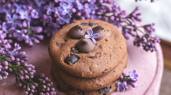 Decorative composition with a Bouquet of lilacs in a light kitchen interior. Clay cup of tea and chocolate cake. A bouquet of lilacs in a vase. Spring floral background with lilacs. Aesthetics